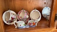 Four floral teacup and saucer sets and the double-handled spoon holder displayed in cabinet