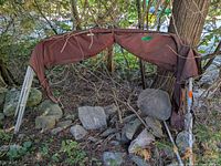 Full view of folded bimini top with brown fabric draped over aluminum frame, rocks and tree for scale