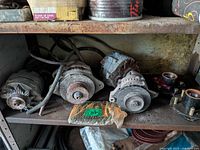 Shelf with three alternators and sealed package, showing rust and dust