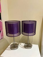 Two identical purple-shade table lamps on white surface