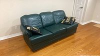 Front angled view of dark green leather three-seat sofa with two pillows