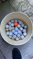 Top view of bucket showing used golf balls including one orange ball
