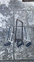 All three saws laid out on stone surface: two hacksaws, one vintage bow saw