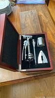 Open wooden box showing five silver-tone wine tools fitted in foam insert