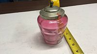 Side view of cranberry glass jar with lid showing color and measuring tape for scale