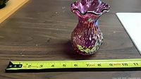 Full view of cranberry glass vase beside tape measure