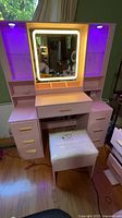 Full view of pink vanity table, LED mirror, side cabinets illuminated purple, stool in front