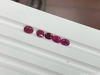 Five oval faceted rubies aligned on white surface