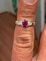Ring on finger showing oval ruby and cubic zirconia accents in sterling band