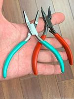 Both pliers in hand: straight teal-grip and bent red-grip