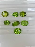 Seven green faceted stones on white grooved tray, top view