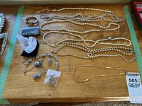 Group of jewellery on tabletop including pearl strands, watch, cufflinks case, porcelain bracelet and brooch, bar-link chain, earrings bag