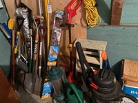 Overall view of assorted shovels, string trimmer, shop vac, bird feeders, extension cord