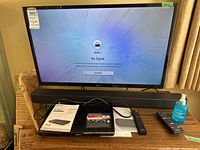 Front view of 32-inch TV on stand with sound bar, DVD player, remotes and wall-mount manual visible