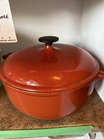 Orange Le Creuset Dutch oven with lid on cabinet shelf
