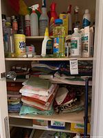 Full closet view showing folded linens on lower shelves and numerous cleaning product bottles and wipes on upper shelves