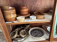 Cabinet shelf with wooden bowls, ramekin, custard cup, rattan basket, stoneware bowls and plates