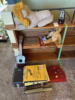Overview of shelf with ukulele, cornet case, plush animals, books, Japanese Ball Game, metronome, etc.
