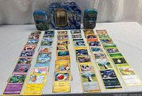 Overview of all cards laid out in four rows with three Pokémon tins