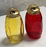 Front view of both glass shakers showing amber and red colors with gold lids
