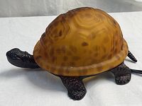 Side view of turtle lamp showing amber mottled glass shell and textured head, leg, tail base