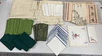 Overview of folded lace tablecloths, assorted napkins, embroidered linens and packaged placemats