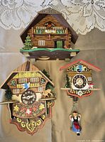 Front view of three wooden chalet style decorative cuckoo clock pieces