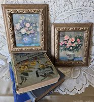 Two framed floral paintings and three vintage books displayed on lace