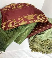 Stack of red and green brocade fabrics showing patterns and fringe