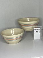 Two striped yellow ware bowls side by side on plain background