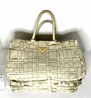 Front view of beige woven Prada handbag with logo plaque