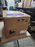 Sealed shipping carton on table; hazardous goods and orientation symbols visible