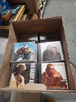 Open cardboard box showing top layer of CDs with visible titles