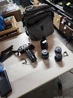 Overall view: camera with attached lens, four additional lenses, grey camera backpack