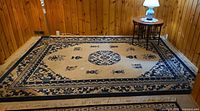 Full view of beige and navy Oriental area rug placed on floor showing overall pattern and fringe