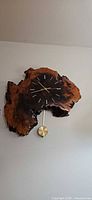 Front view of live-edge redwood burl wall clock showing dial, brass hands and pendulum