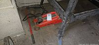 Side view of red hydraulic floor jack under table