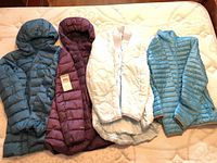 Group shot of four women’s puffer jackets laid out on bed