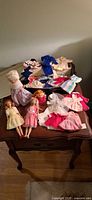 Overview of three dolls and multiple clothing pieces on tabletop