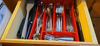 Drawer with red organizer holding assorted flatware, serving spoons, turner spatula and tongs