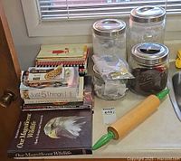 Overall lot showing stack of cookbooks, four Mason jars and wooden rolling pin