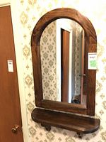Full view of arched-top mirror with shelf mounted on wall