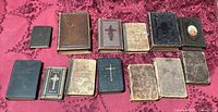 Group shot of all thirteen small antique bibles and missals on red cloth