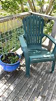 Full view of green Adirondack chair next to blue planter on deck