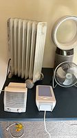 Group showing oil-filled radiator, compact heater, Dyson tower, desk fan, SAD lamp