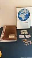 Atlas, Himalayas book, two US $2 bills, assorted coins displayed