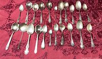 All 22 sterling spoons laid out on red cloth