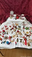 Full view of approximately 60 assorted vintage Christmas ornaments laid out on white cloth