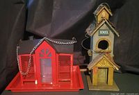 Overall view of red metal bird feeder and wooden schoolhouse birdhouse