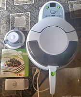Top view of T-fal Actifry air fryer, Pampered Chef measuring cup, Actifry booklet and burger press